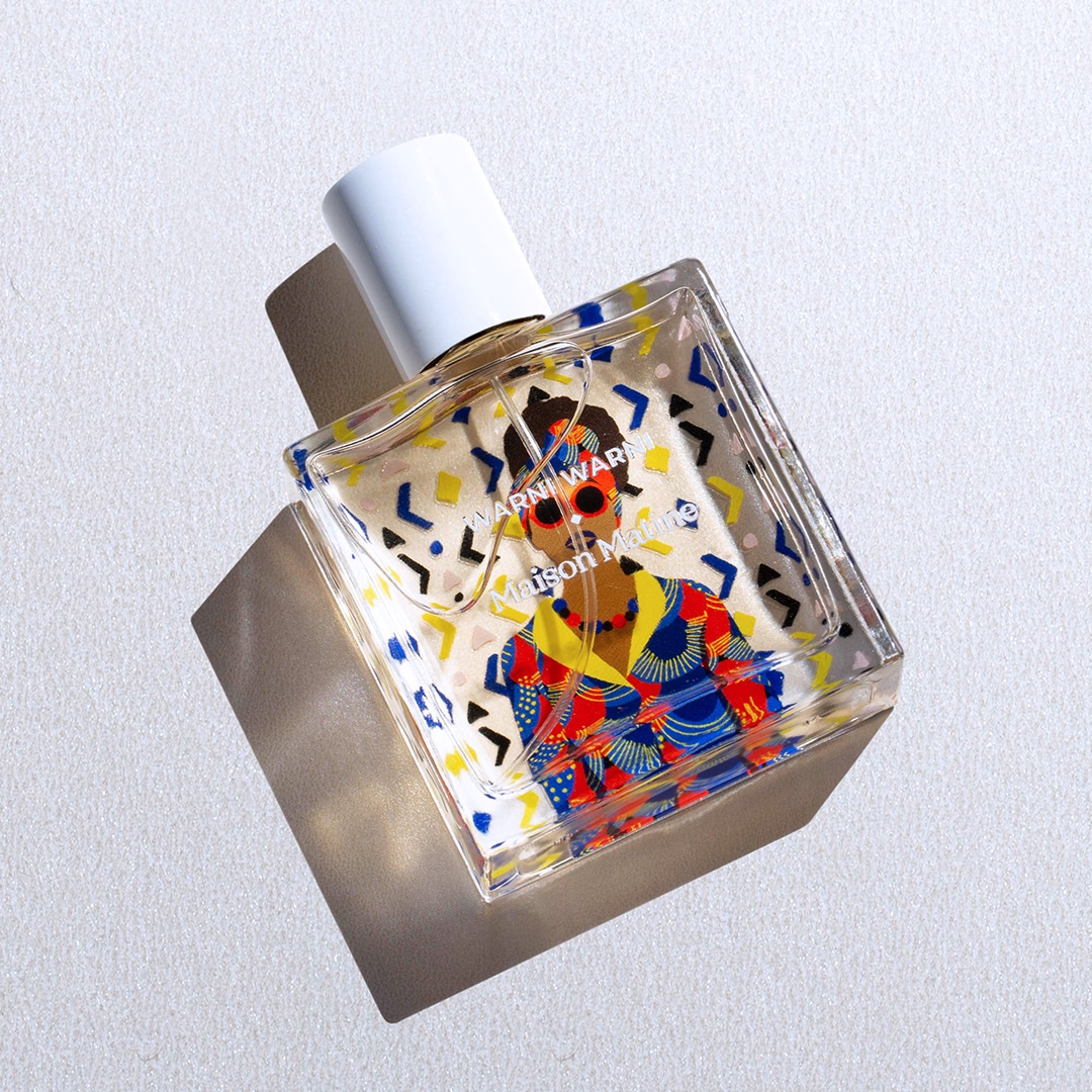 Abgebildet ist der Parfumflakon Warni Warni von Maison Matine. Der rechteckige Glasflakon trägt eine farbenfrohe Illustration in Rot, Blau, Gelb und Schwarz, die typisch für die künstlerische Gestaltung der Marke ist. Das Foto zeigt den Flakon leicht schräg liegend auf hellem Untergrund, wodurch sich ein markanter Schatten abzeichnet.