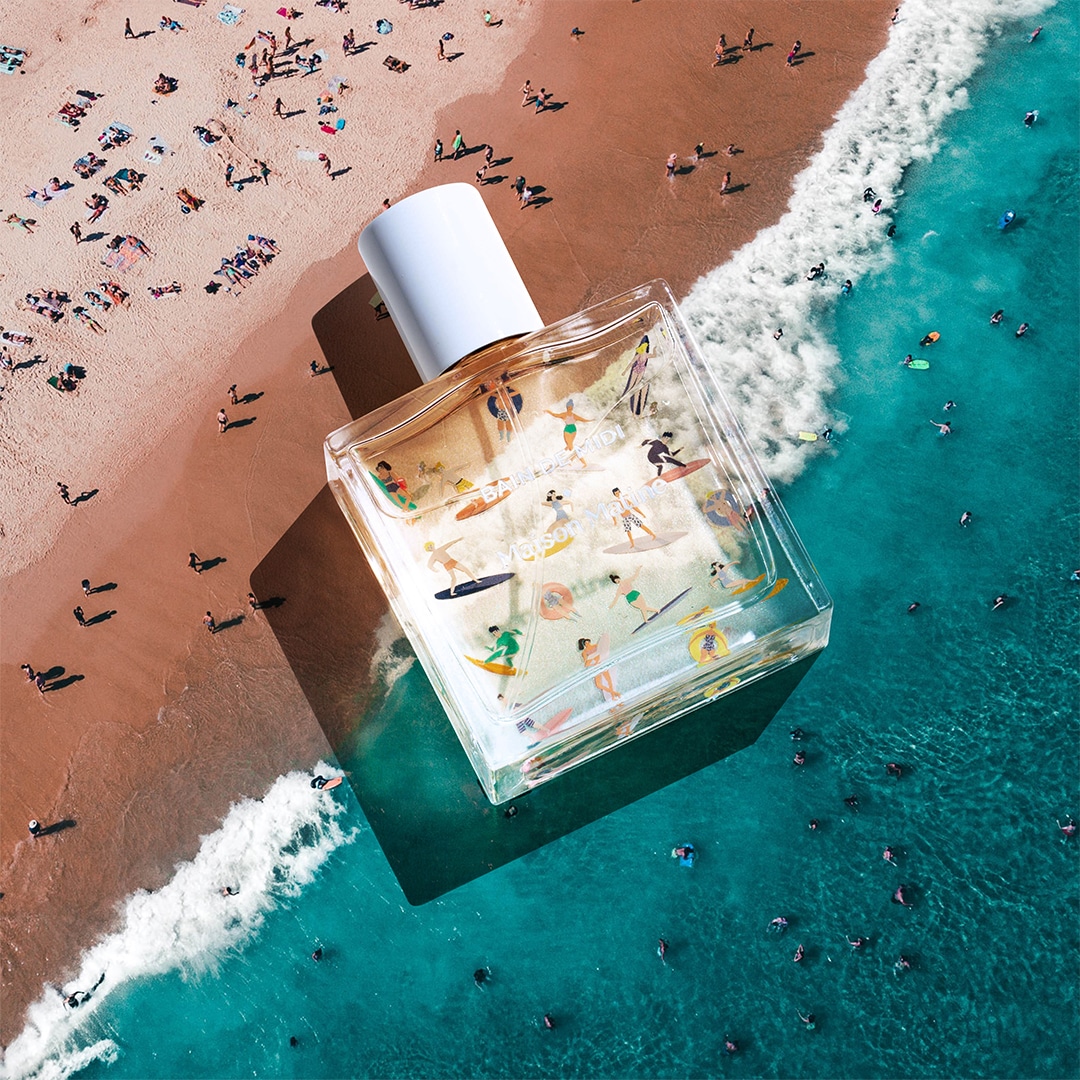 Flakon von Maison Matine Bain de Midi liegt auf einer Strand-Szene mit türkisblauem Meer und vielen Menschen im Wasser und am Sandstrand. Die Illustration auf dem Glas zeigt bunte Figuren beim Surfen und Sonnenbaden und vermittelt spielerisch das sommerlich-leichte Lebensgefühl des Duftes.