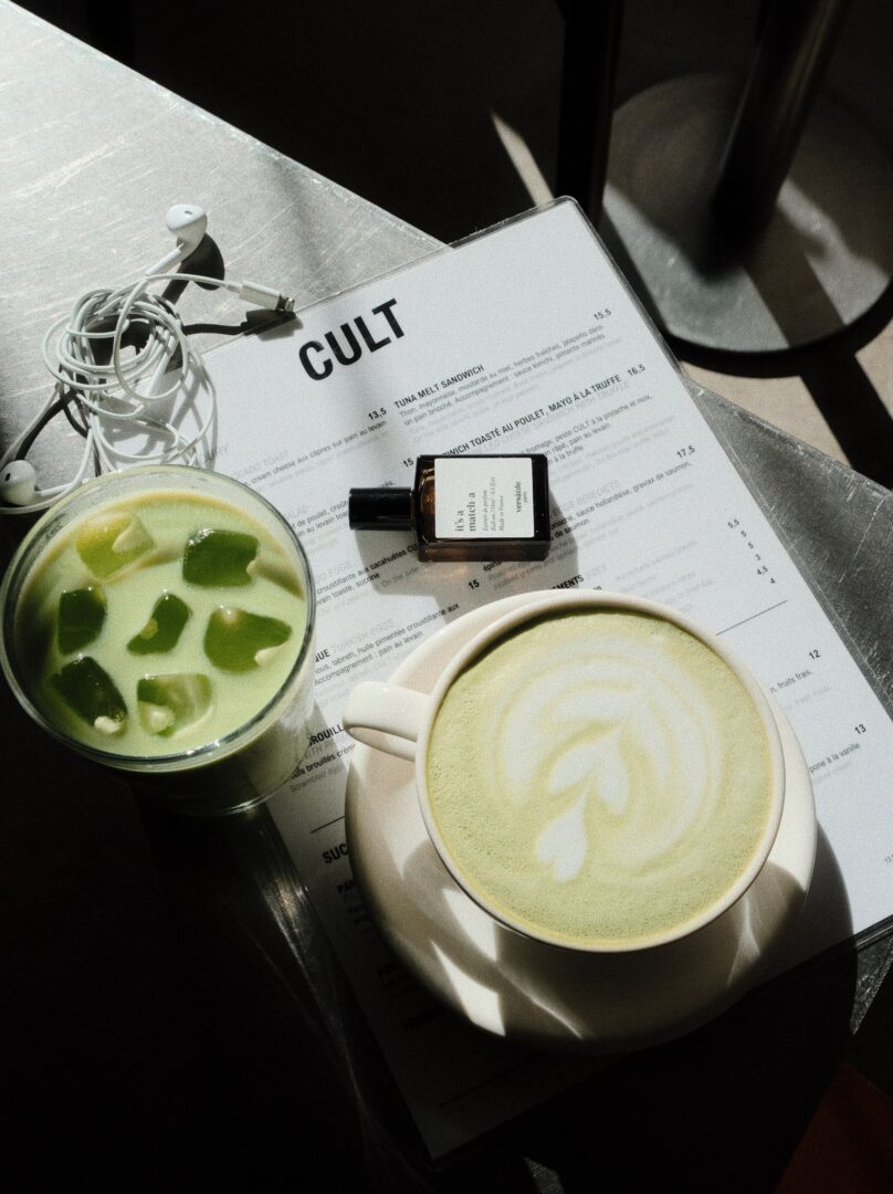 Versatile It’s a Match-A Parfum im Roll-on auf einem Café-Tisch, daneben ein heißer Matcha Latte und ein kalter Matcha Drink