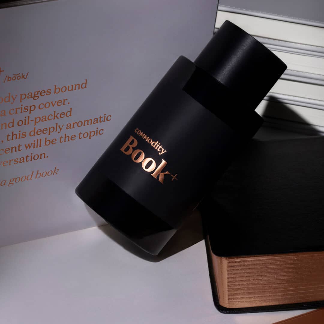 Commodity Book Parfum Plus – schwarzer Flakon vor aufgeschlagenem Buch mit goldener Schrift, intensive Duftvariante