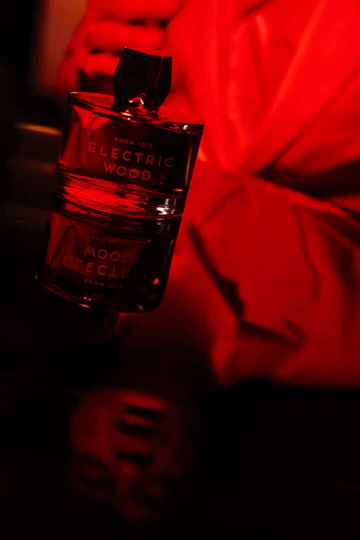 Flakon von Room 1015 Electric Wood Extrait de Parfum in rotem Licht, reflektiert auf glänzender Oberfläche – Sinnbild für Hitze, Leidenschaft und musikalische Energie.