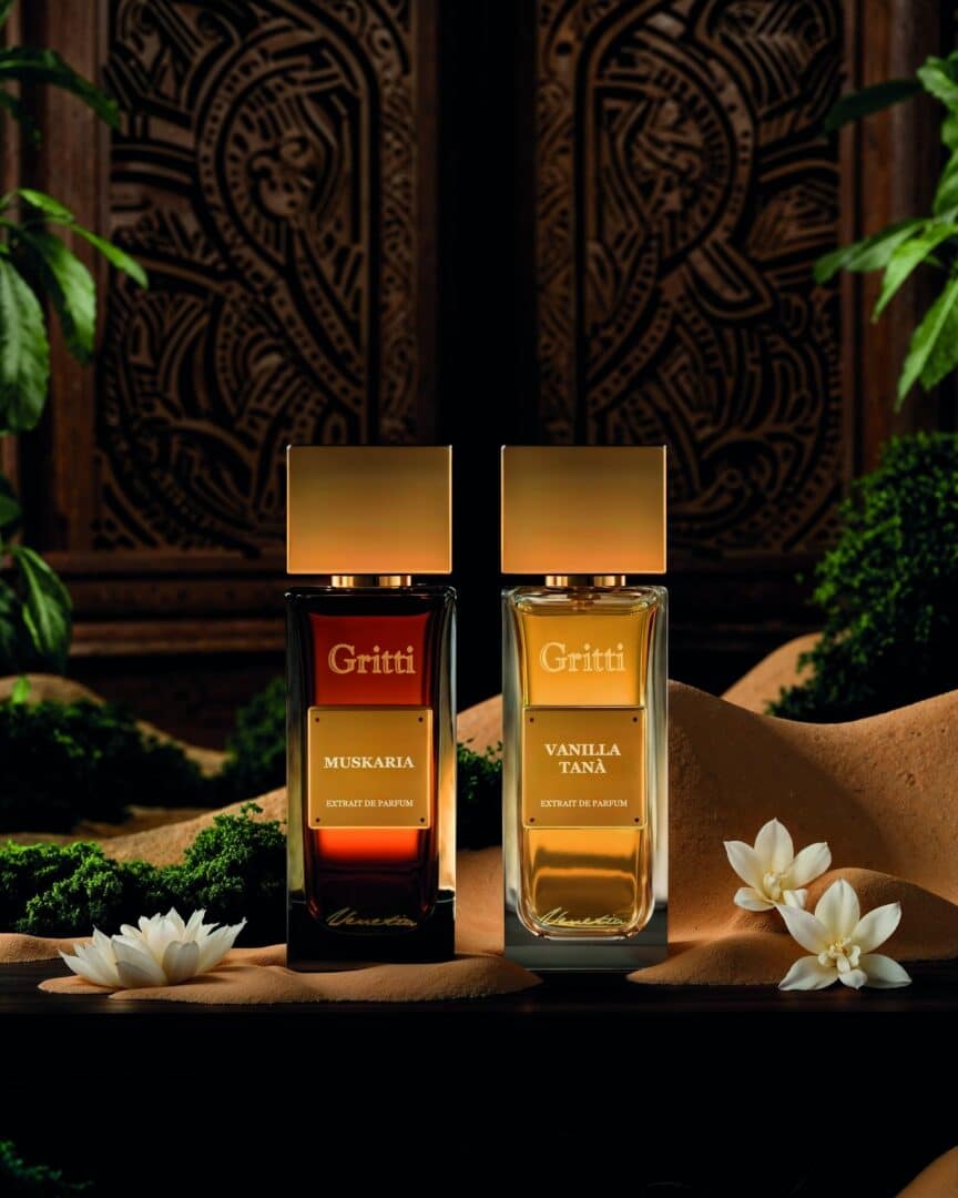 Gritti Ivy Collection – Flakons von Muskaria und Vanilla Tanà auf sandfarbenem Untergrund mit weißen Blüten