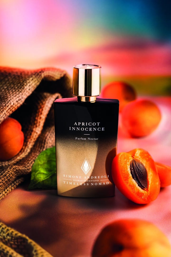 Flacon of Apricot Innocence from the Timeless Nomad Collection by Simone Andreoli, surrounded by ripe apricots against a colorful, bright summery background.