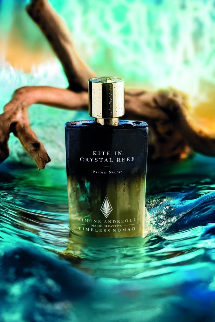 Flacon of Kite in Crystal Reef from the Timeless Nomad Collection by Simone Andreoli, staged on turquoise blue water against a backdrop of waves and driftwood.