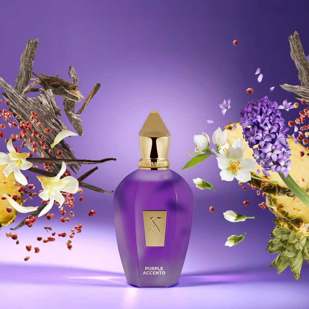 Xerjoff Purple Accento Flakon in kräftigem Violett mit goldener Kappe, umgeben von Ananas, Hyazinthen, Jasminblüten, rosa Pfeffer und Oud-Holz auf violettem Hintergrund.