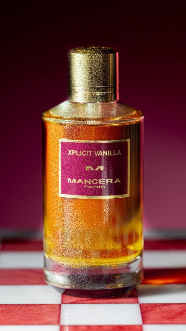 Nahaufnahme des Flakons von Mancera Xplicit Vanilla auf rot-weiß kariertem Hintergrund, mit feinen Wassertropfen und intensiver Lichtreflexion.