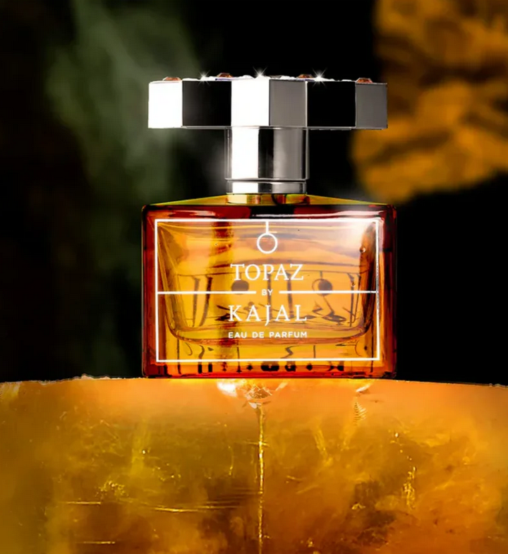 Flakon von Topaz by Kajal, glänzend und bernsteinfarben, vor einem dunkel-grünen und goldenen Hintergrund, der an den Schimmer eines Topas-Edelsteins erinnert.