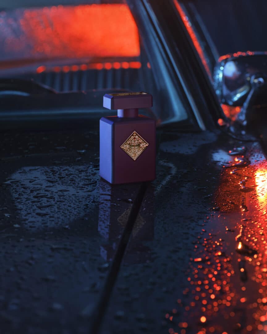 Flakon von Can’t get Enough von Initio Parfums Privés auf regennasser Motorhaube, stimmungsvolles Licht in Blau und Rot.