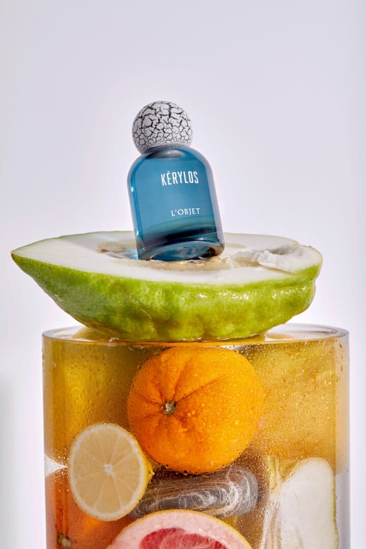 Flakon von Kérylos von L’Objet auf einer halbierten Zitrusfrucht, umgeben von weiteren frischen Zitrusfrüchten in einem Glasgefäß.