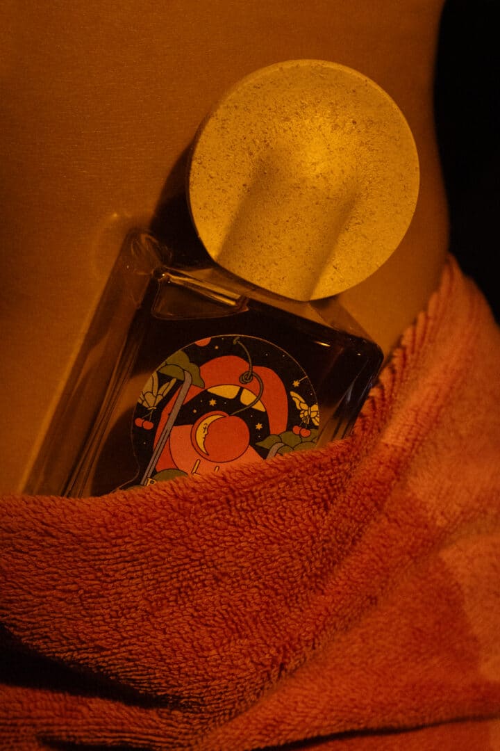 Bain de Minuit aus der Night Fever Collection von Maison Matine – Parfumflakon in warmem Licht mit Textilien