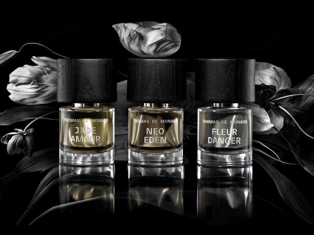 Drei Parfumflakons der Artist Collection von Thomas de Monaco – Jade Amour, Neo Eden und Fleur Danger – vor schwarzem, floralen Hintergrund.