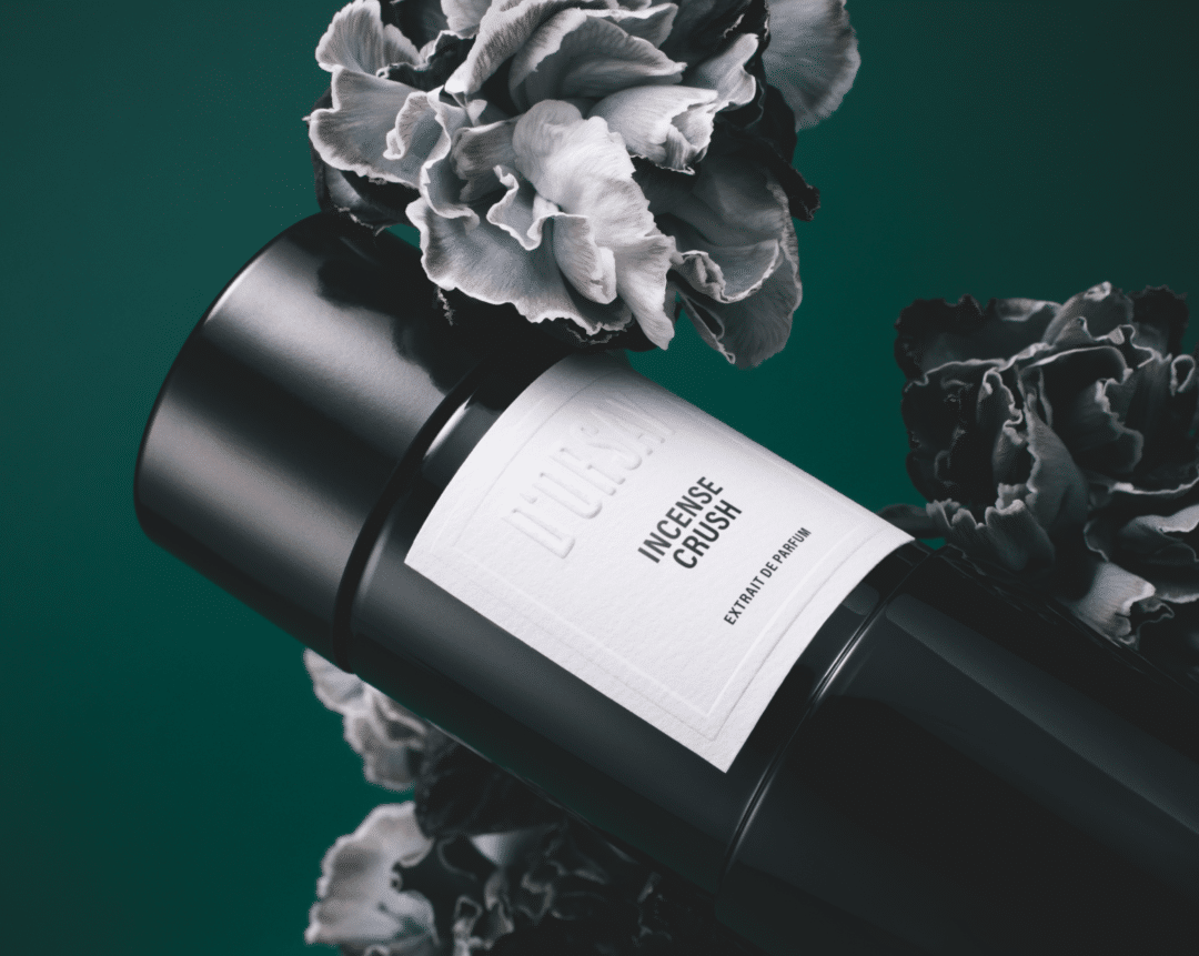 Flakon von Incense Crush von D’Orsay Extrait de Parfum, inszeniert mit dunklen Blüten vor tiefgrünem Hintergrund