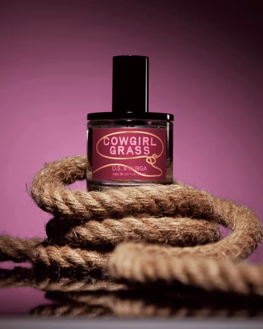 Cowgirl Grass von D.S. & Durga – Western-inspirierter Nischenduft mit Kräutern und Gräsern Cowgirl Grass von D.S. & Durga – Parfumflakon auf grobem Seil vor violettem Hintergrund, inspiriert vom amerikanischen Westen
