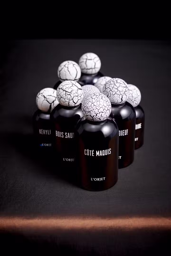 L’Objet Parfums – Kollektion mit skulpturalen Flakons und rissigen Kugelverschlüssen Flakons der L’Objet Parfumkollektion mit charakteristischen, rissigen Kugelverschlüssen, arrangiert vor dunklem Hintergrund – Côté Maquis, Bois Sauvage und weitere Düfte