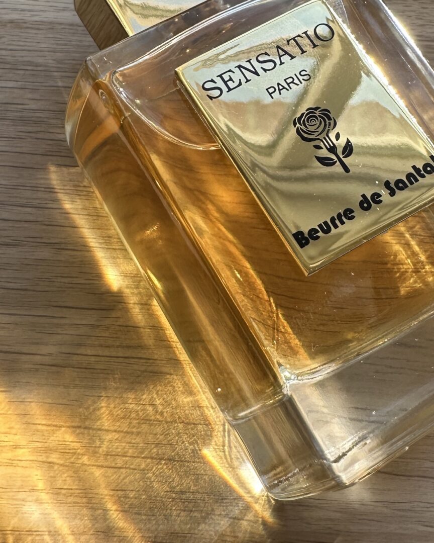 Beurre de Santal von Sensatio Paris Flakon im warmen Sonnenlicht mit goldenen Reflexen auf Holzoberfläche