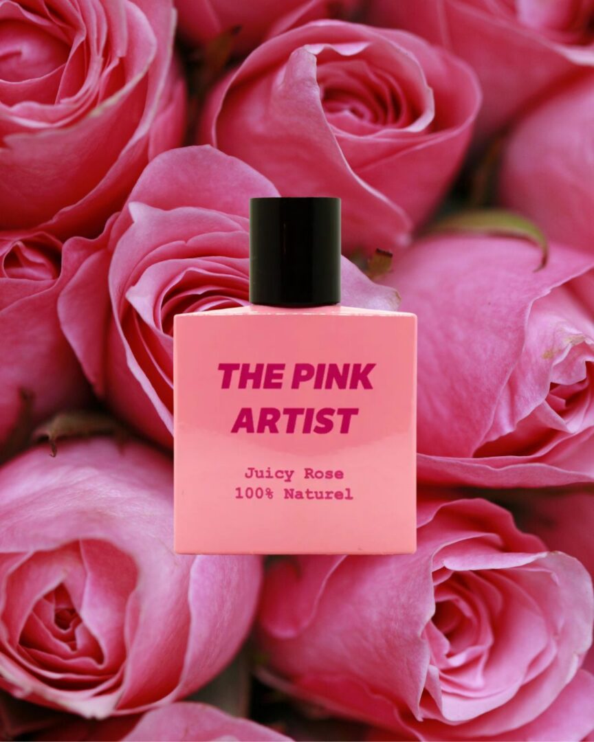 The Pink Artist Juicy Rose Parfumflakon vor pinken Rosenblüten – fruchtiger Rosenduft