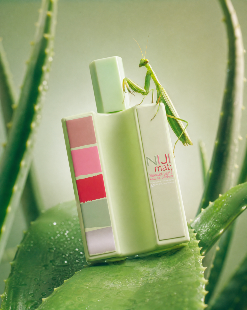Flakon von Nu mat; by Masakï Matsushïma auf einem Aloe-vera-Blatt, begleitet von einer grünen Gottesanbeterin in einer frischen, grünen Naturkulisse.