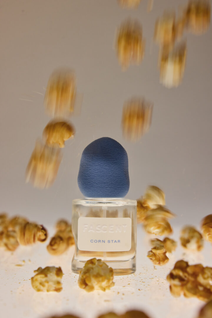 Flakon von Fascent Corn Star mit blauer Verschlusskappe, umgeben von herabfallendem Popcorn.