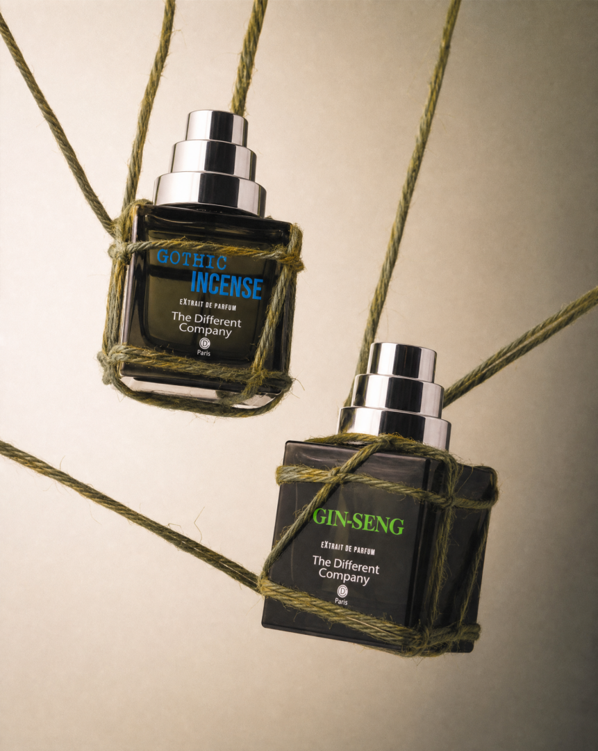 Zwei Extrait de Parfums aus der Extraits-Extrêmes-Kollektion von The Different Company – Gothic Incense und Gin-Seng – schweben, von olivgrünen Seilen umwickelt, vor einem warmen beigefarbenen Hintergrund. Die schwarzen Flakons mit silbernen Verschlüssen setzen mit ihren leuchtend blauen und grünen Schriftzügen markante Farbakzente und verleihen der minimalistischen, editorialen Inszenierung eine moderne, grafische Wirkung.