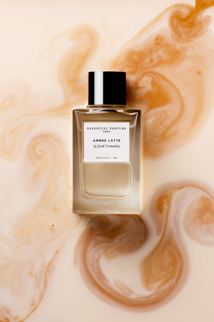 The Ambre Latte bottle by Essential Parfums against a cream-colored background with marbled swirls of coffee and milk foam.