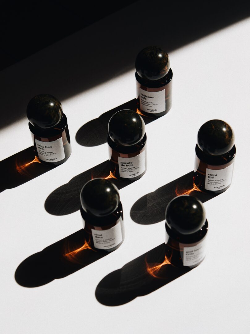 Mehrere Parfumflakons von Versatile Paris mit kugelförmigen Verschlüssen, arrangiert im starken Licht-Schatten-Kontrast.