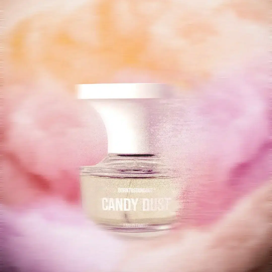 Flakon von Candy Dust von BORNTOSTANDOUT, umgeben von weich verschwommener rosa Zuckerwatte vor pastellfarbenem Hintergrund.