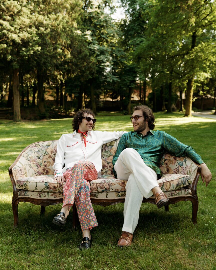 Francesco und Piergiacomo Sigalini, Gründer von Pantamolle, in farbenfrohen Outfits auf einem Sofa im Garten