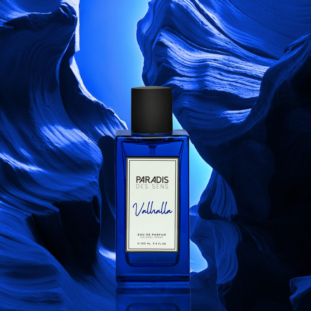 A blue "Valhalla" bottle by Paradis des Sens set against an abstract, blue-lit rocky backdrop.