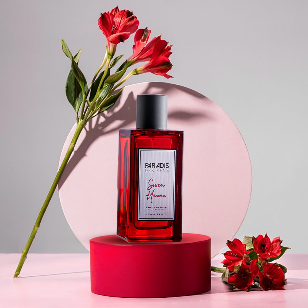Roter Flakon von Seven Heaven von Paradis des Sens auf einem Podest, umgeben von roten Blüten.