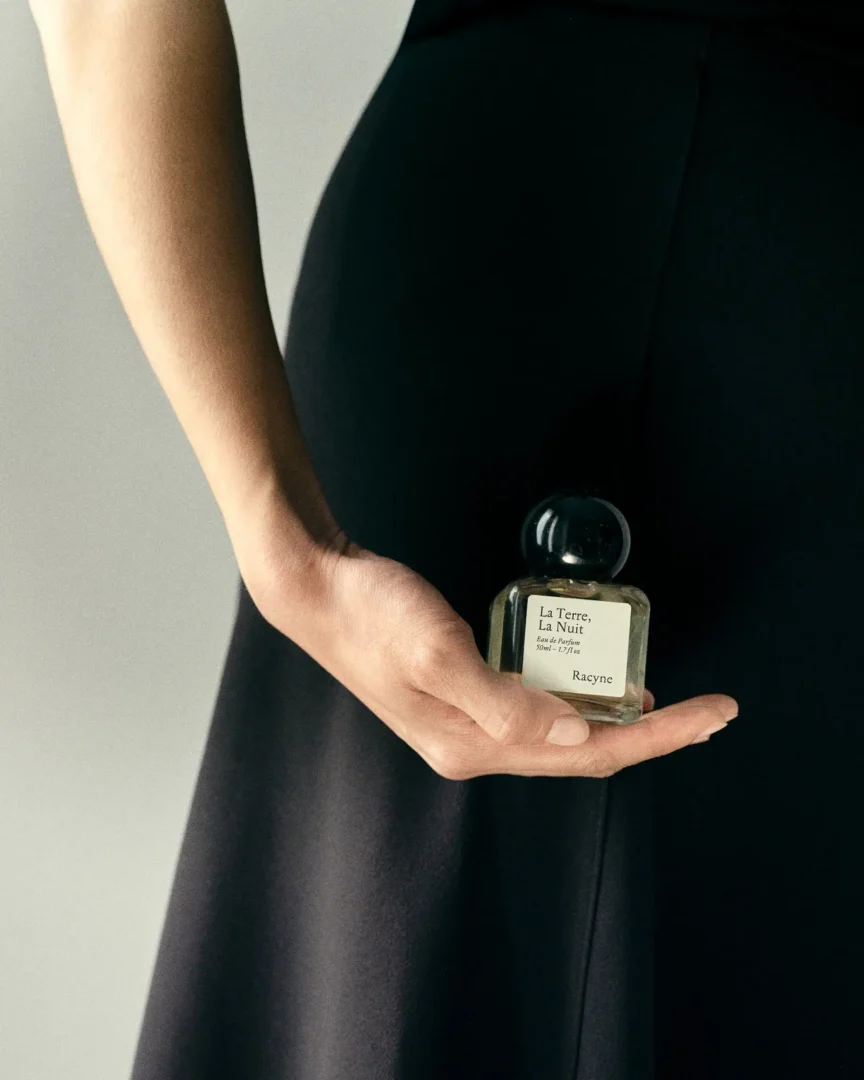 Racyne – La Terre, La Nuit Racyne La Terre, La Nuit in der Hand einer Person vor einem schwarzen Kleid