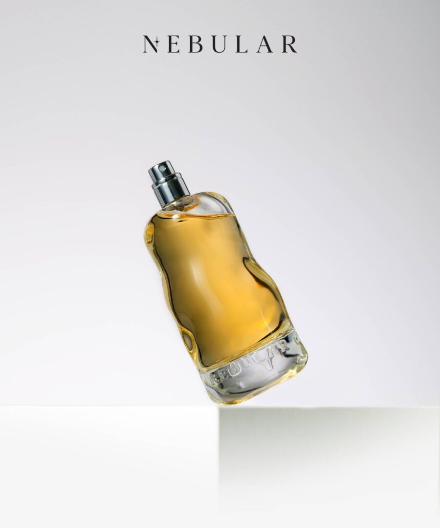 Goldfarbener Parfumflakon von Nebular Parfums, schräg auf einer weißen Kante balancierend vor hellem Hintergrund.