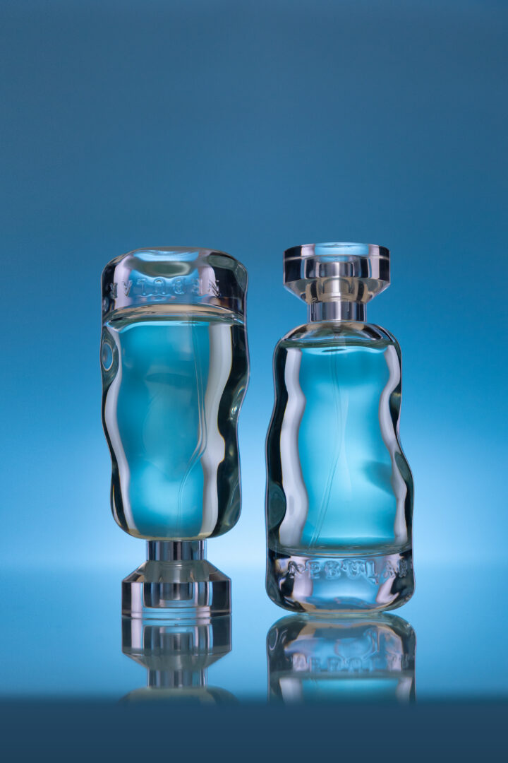 Two turquoise Nebular perfume bottles against a blue background, one standing upright and the other mirrored upside down.